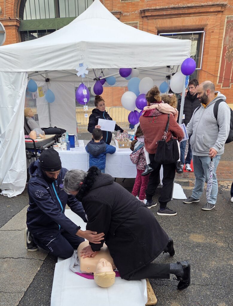 Sablés faits maison et estampés du logo VYV pour la vente du Téléthon.-Un citoyen participe au fil rouge "massage cardiaque" sur le stand VYV Ambulance, encadré par un collaborateur.
